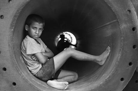 Grayscale photo of boy in crew neck t shirt sitting in round pipe