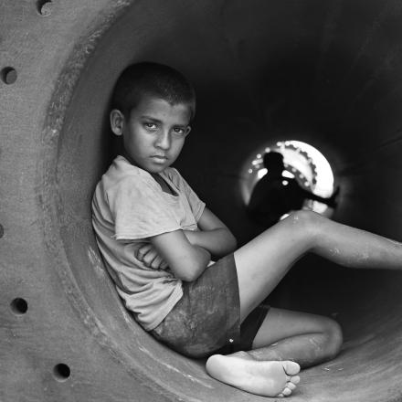 Grayscale photo of boy in crew neck t shirt sitting in round pipe