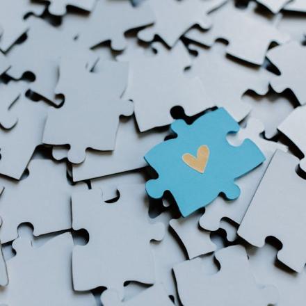 A single blue puzzle piece with a heart amid scattered pieces, symbolizing connection.
