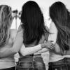Three women in jeans and tops bonding at the beach in grayscale.