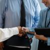Crop unrecognizable diverse partners in formal clothes with documents shaking hands during business meeting in office